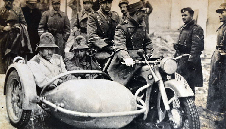 Ελληνοϊταλικός πόλεμος 1940-41. Στην πίσω πλευρά της φωτογραφίας αναγράφεται: Κάπου από το μέτωπον. Ένας Ιταλός Συνταγματάρχης των Αλπινιστών και ο λοχαγός υπασπιστής του αιχμάλωτοι του Ελληνικού στρατού μεταφερόμενοι εις τα μετόπισθεν 
